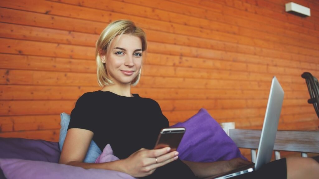 Young Woman Smiling Holding Phone Laptop On Lap