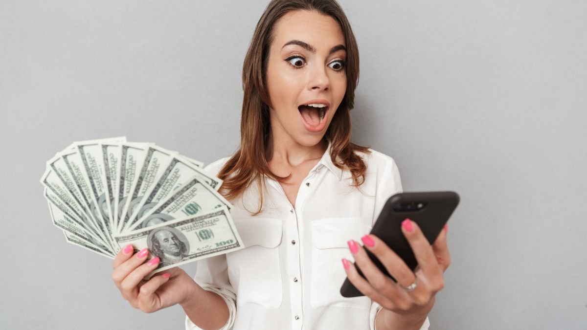 Shocked Woman Looking At Phone While Holding Money
