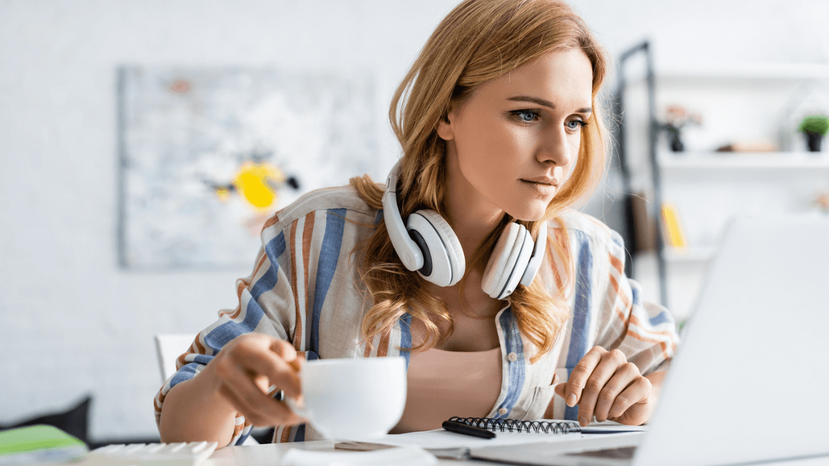 Woman holding cup and working with laptop